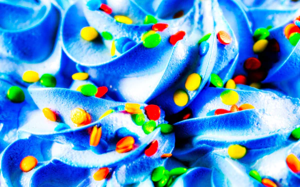 HD PC desktop wallpaper: close-up of bright blue ice cream swirls topped with colorful Smarties candy sprinkles — vibrant sweets food background.