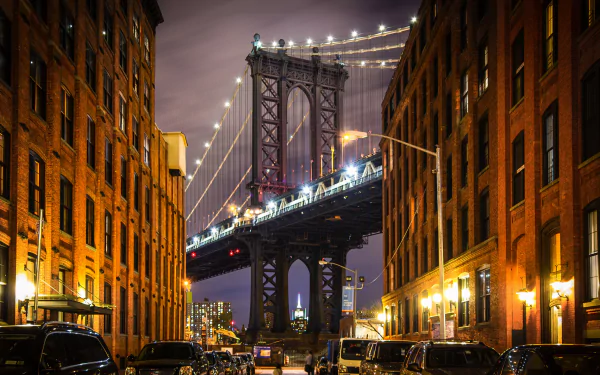 Night view of Manhattan Bridge framed by illuminated buildings in New York, creating a striking HD desktop wallpaper showcasing urban architecture and city lights.