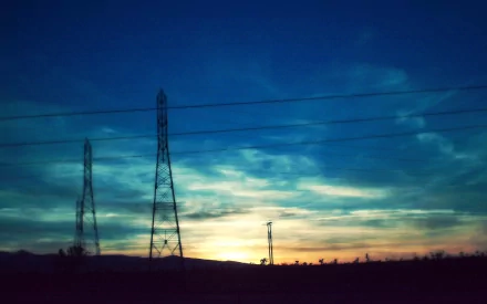HD desktop wallpaper featuring silhouetted power line towers against a vibrant sunset sky, highlighting man-made structures in a natural landscape.