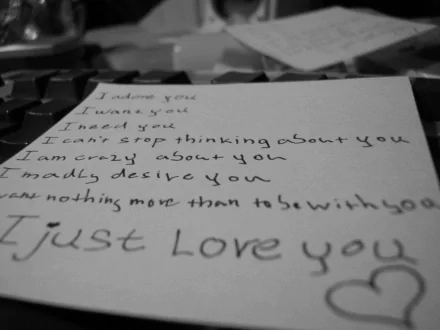 HD desktop wallpaper with an artistic black-and-white photograph of a handwritten love note. The note expresses deep affection with phrases like I adore you and I just love you.