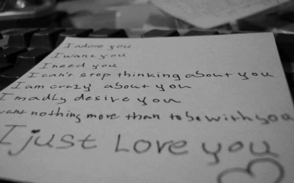 HD desktop wallpaper with an artistic black-and-white photograph of a handwritten love note. The note expresses deep affection with phrases like I adore you and I just love you.