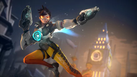 HD PC desktop wallpaper featuring Tracer from the video game Overwatch in an action pose with futuristic pistols and a blurred city backdrop.