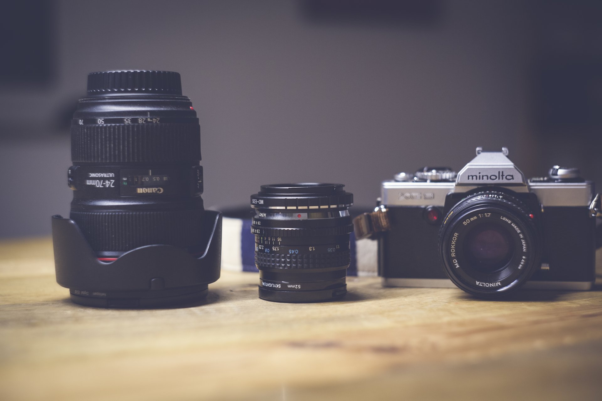 A 4K Ultra HD wallpaper featuring a Canon lens, a Minolta camera, and an additional lens arranged on a wooden surface against a blurred background.