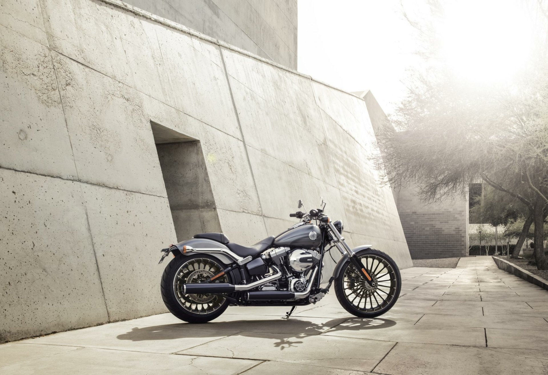 HD PC desktop wallpaper showing a Harley-Davidson Breakout motorcycle parked by a modern concrete wall in soft sunlight.