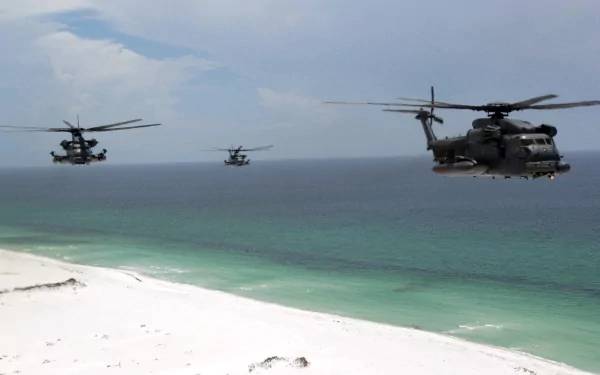Three Sikorsky MH-53 military helicopters fly in formation over a pristine beach with turquoise waters, under a partly cloudy sky. HD desktop wallpaper and background.