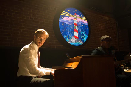 Ryan Gosling sits at a piano in a dimly lit setting, with a colorful lighthouse mural behind him, capturing a moment from the movie La La Land. This HD image serves as a striking desktop wallpaper.