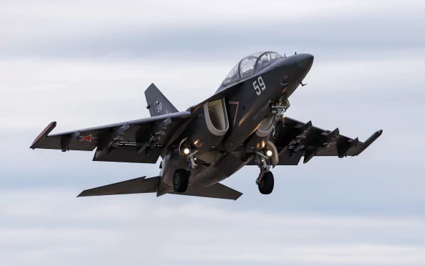 Military Yakovlev Yak-130 jet fighter warplane captured mid-flight against a cloudy sky in this HD desktop wallpaper and background.