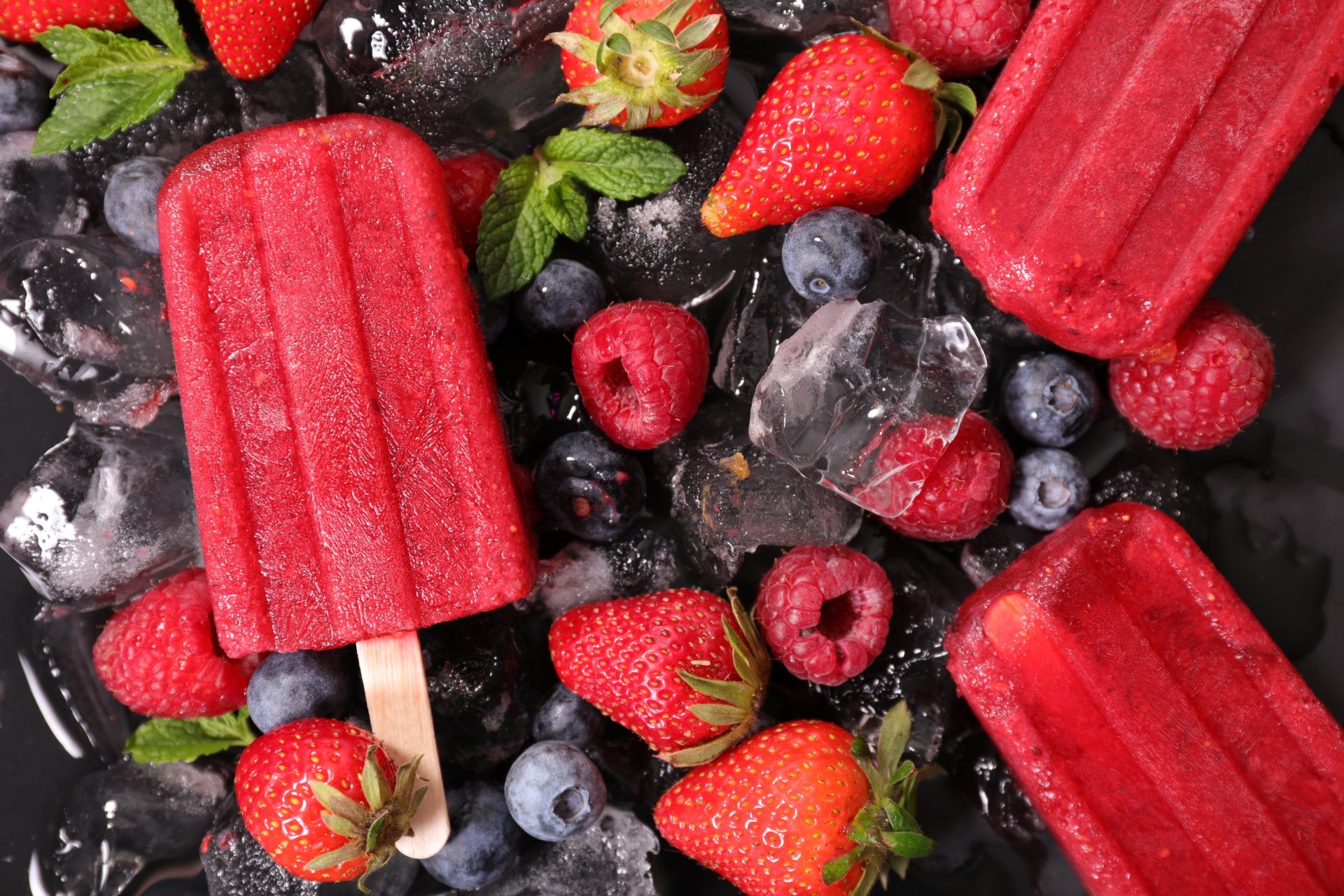 Vibrant 8K Ultra HD wallpaper featuring blackberry, raspberry, blueberry, and strawberry popsicles with fresh berries and ice cubes on a dark background.