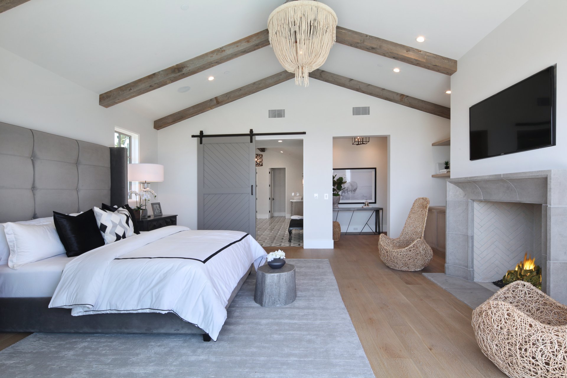Modern bedroom with vaulted ceiling, wooden beams, a large bed, fireplace, and stylish furniture, captured in 4K Ultra HD for PC desktop wallpaper use.