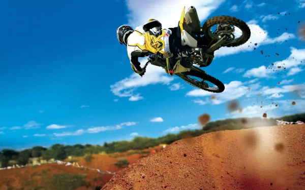 A motocross rider performs an impressive jump against a clear blue sky, with dirt flying beneath the motorcycle, showcasing the thrill of off-road biking in this HD desktop wallpaper.