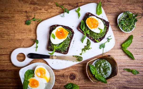4K Ultra HD still life of toasted bread topped with soft-boiled eggs and green herbs on a white cutting board, set on a rustic wooden background.