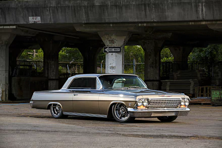 Classic Chevrolet Impala muscle car hot rod with chrome trim and low stance parked beneath an urban overpass — HD PC desktop wallpaper background.