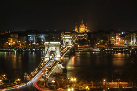 Nighttime time-lapse of Budapest’s Chain Bridge spanning the river, showcasing vibrant city lights and historic architecture in this HD desktop wallpaper.