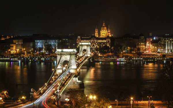Nighttime time-lapse of Budapest’s Chain Bridge spanning the river, showcasing vibrant city lights and historic architecture in this HD desktop wallpaper.