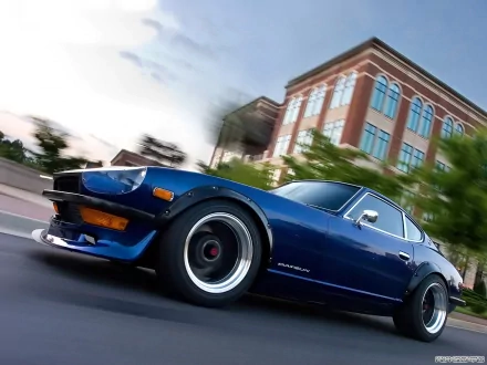 Blue classic Nissan Datsun 240Z sports car in motion, showcasing its iconic JDM design on a city street, captured in HD for a desktop wallpaper background.