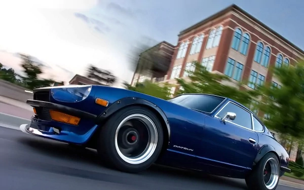 Blue classic Nissan Datsun 240Z sports car in motion, showcasing its iconic JDM design on a city street, captured in HD for a desktop wallpaper background.