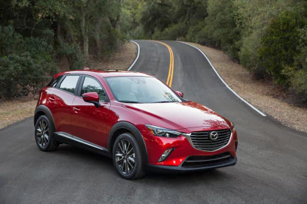 A red Mazda CX-3 SUV parked on a winding road surrounded by trees, shown in a high-resolution 4K Ultra HD PC desktop wallpaper and background.