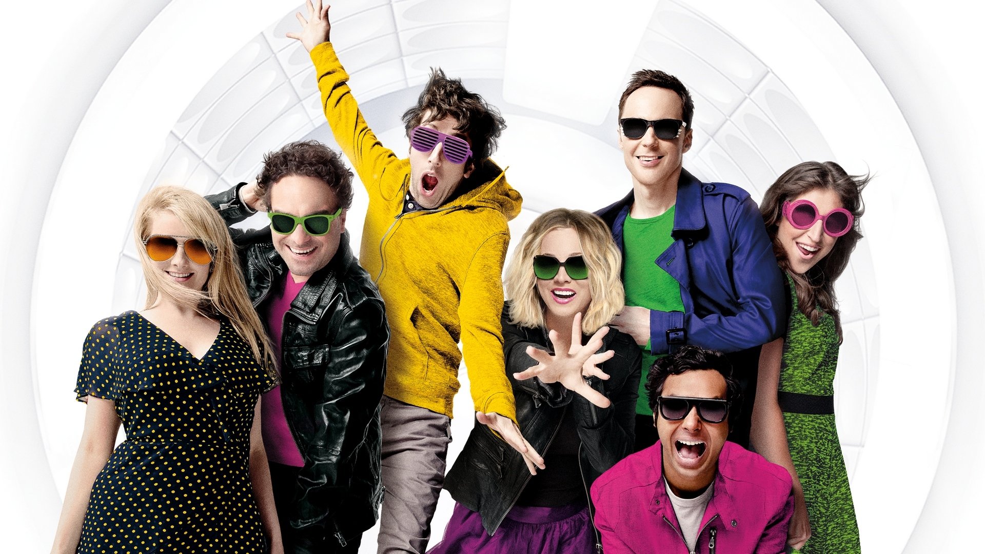 HD desktop wallpaper showing a seven-person TV sitcom ensemble in colorful outfits, posing energetically against a bright circular backdrop.