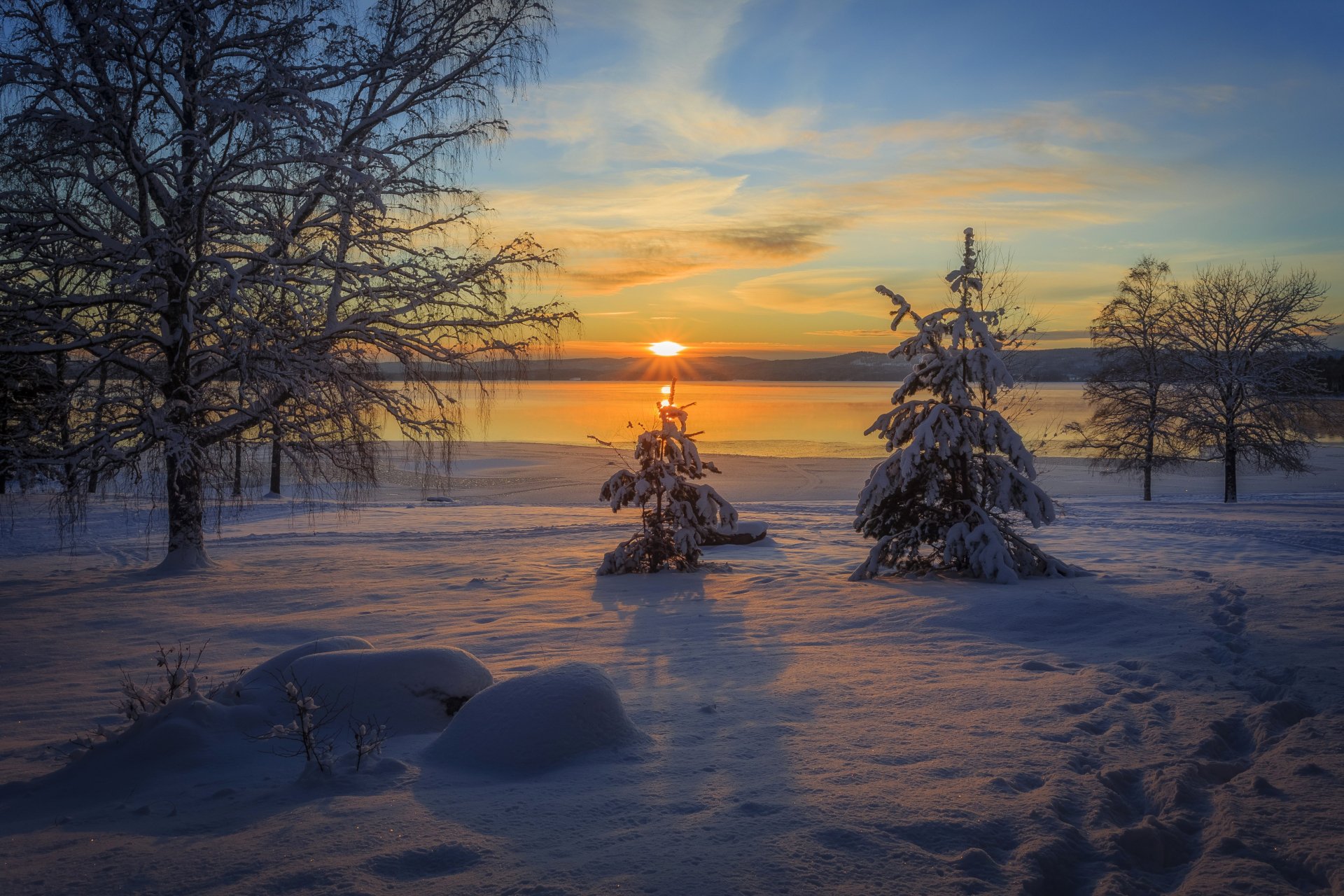 HD desktop wallpaper depicting a winter nature scene of snow-covered trees at sunset, with the sun casting warm hues across a peaceful landscape.
