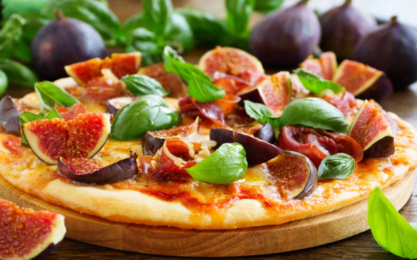HD PC desktop wallpaper showing a fig-topped pizza close-up: fresh figs, basil leaves and melted cheese on a wooden board, vibrant food colors.