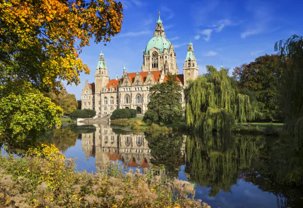 View of Hanover's New City Hall in Germany, showcasing its detailed architecture reflected in a serene body of water, framed by autumn foliage.