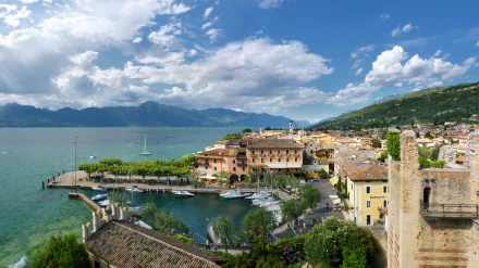 Torri del Benaco, Italy — lakeside village and man-made harbor with boats, tree-lined promenade, terraced houses and mountains; HD PC desktop wallpaper background.