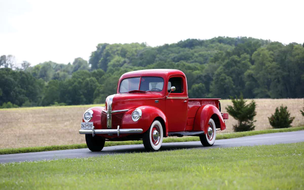 A vibrant red Ford Deluxe Pickup truck drives on a rural road with green grass and trees in the background, captured in stunning 4K Ultra HD for desktop wallpaper.