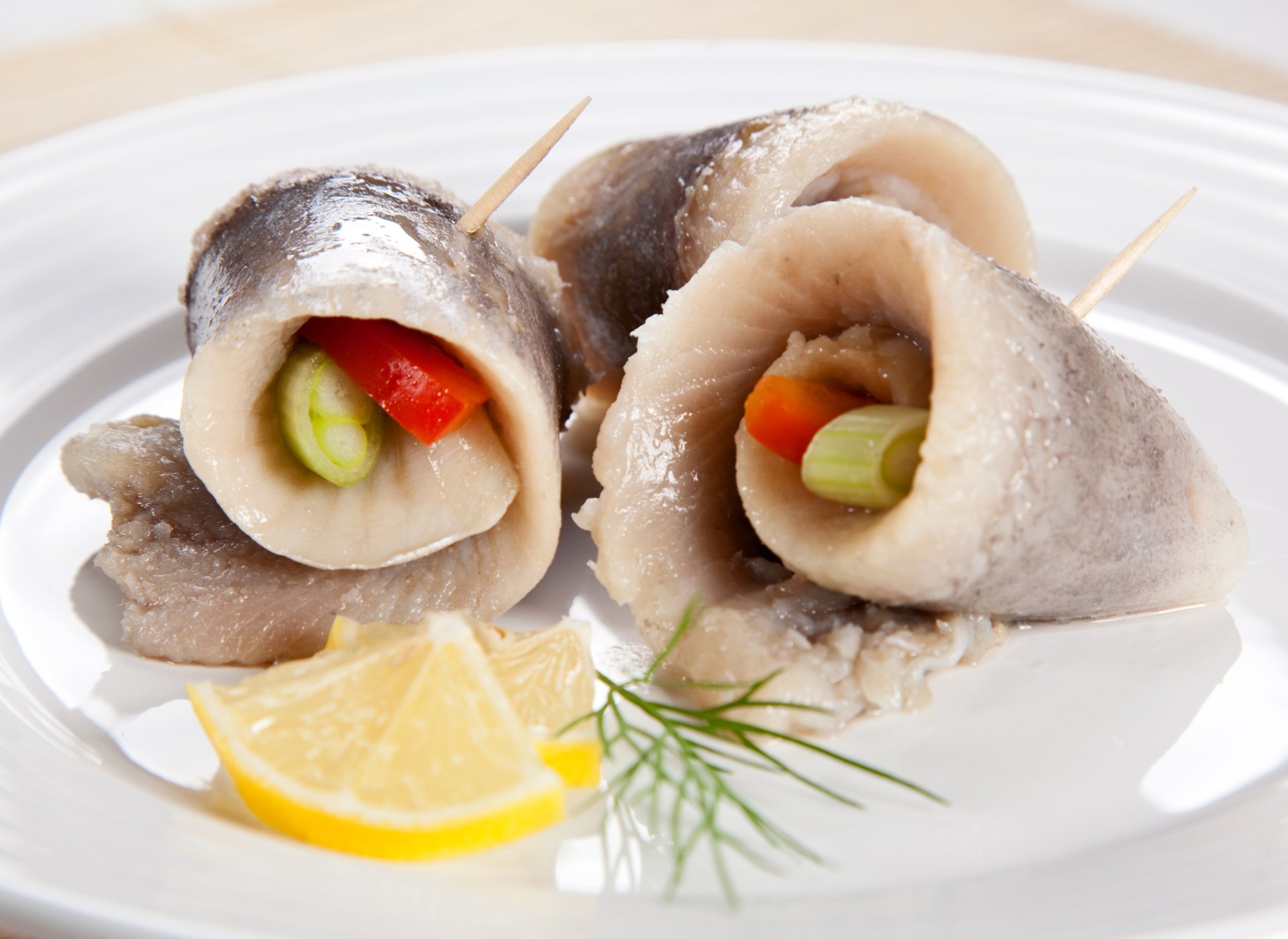 Close-up of rolled fish fillets stuffed with vegetables, garnished with lemon wedges and dill, presented as a vibrant seafood dish in 4K Ultra HD quality.