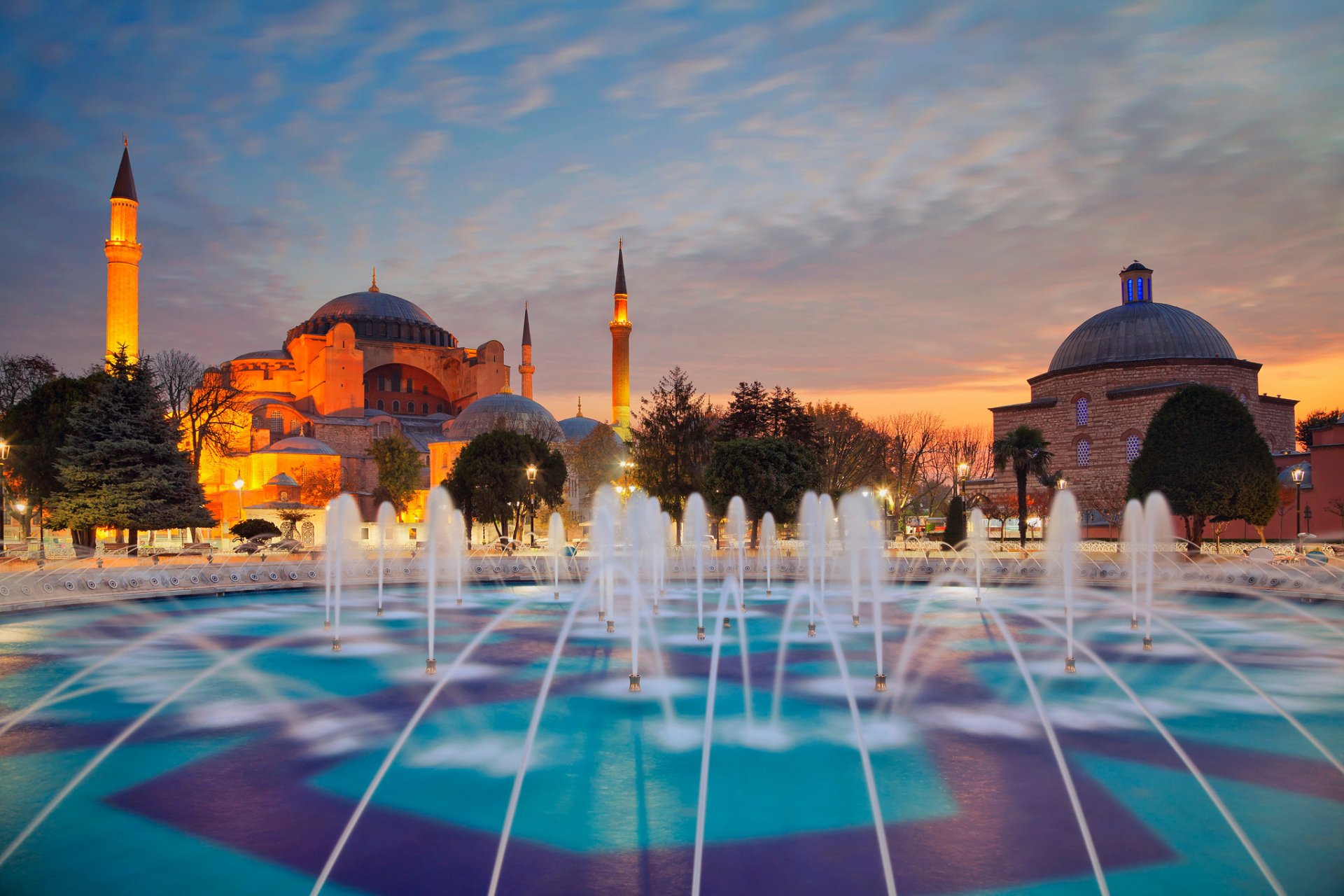 Hagia Sophia and minarets in Istanbul, Turkey, illuminated at evening with a vibrant fountain in the foreground.