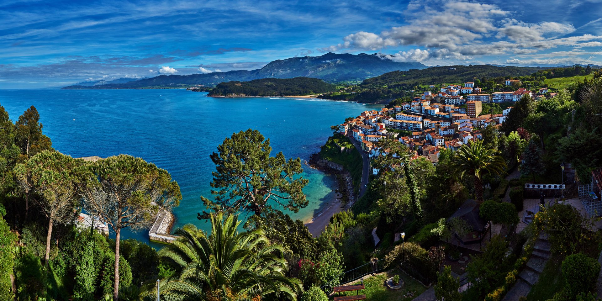 HD desktop wallpaper of a Spanish coastal town with a vibrant ocean, palm trees, houses, and a lush landscape under a blue sky.