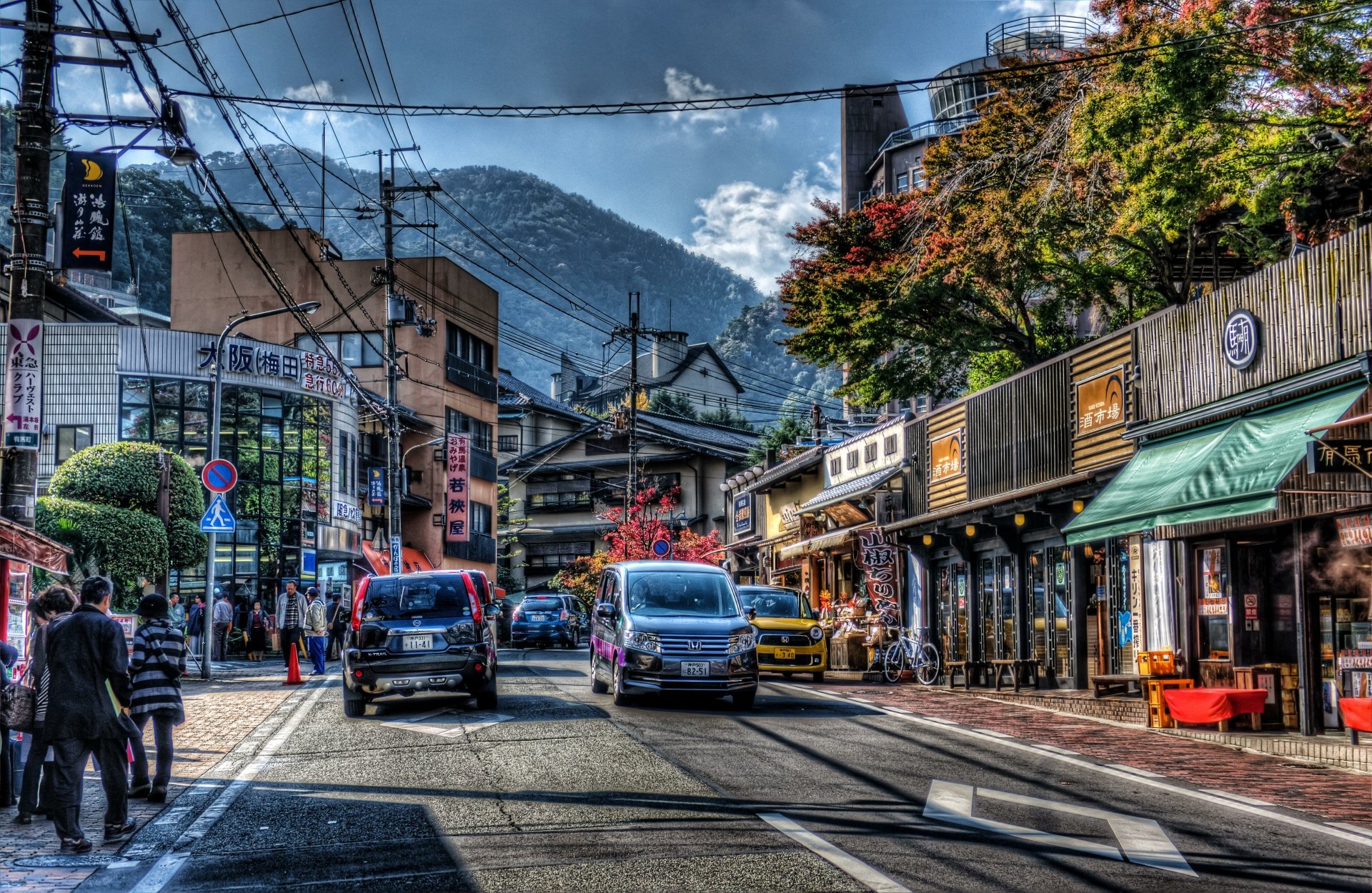 A vibrant street scene in Kobe, Japan, featuring cars on the road, distinctive architecture, and lush greenery against a backdrop of mountains. This HD desktop wallpaper captures the essence of urban life in HDR.