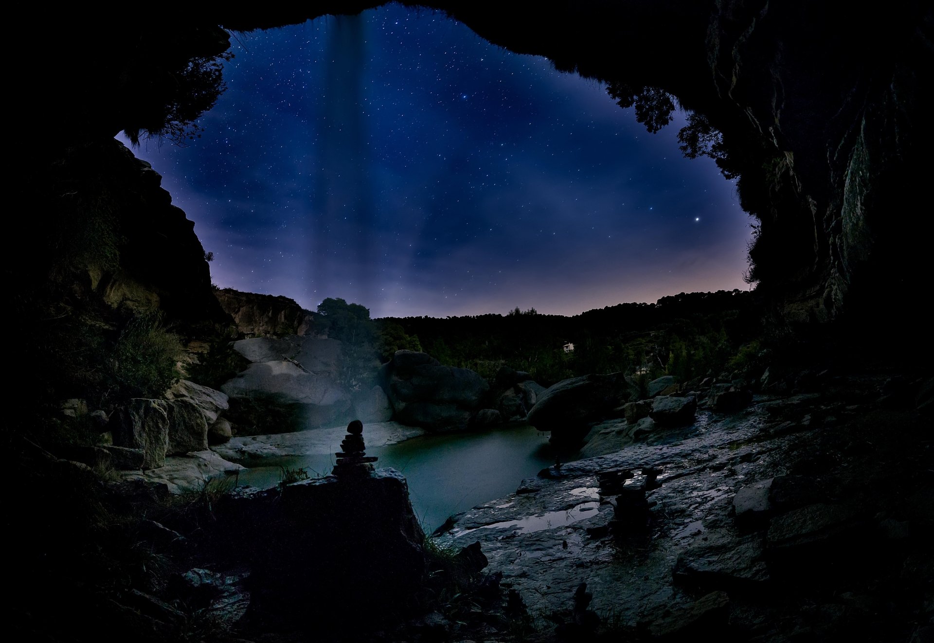 Nighttime view of La Portellada cave in Spain, featuring a starry sky, calm water, and natural rock formations in a 4K Ultra HD desktop wallpaper.