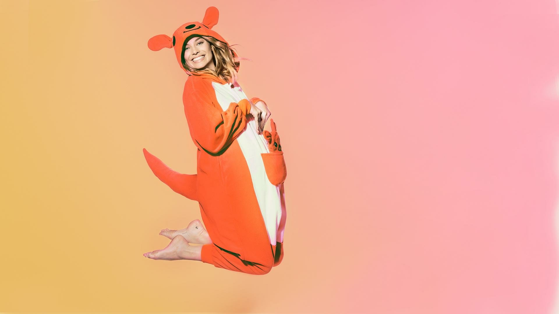 HD PC desktop wallpaper featuring celebrity Margot Robbie wearing a playful red kangaroo onesie against a smooth gradient orange to pink background.
