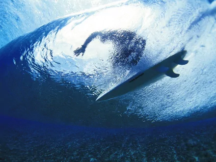 A dynamic underwater view of a surfer gliding beneath a wave, capturing the excitement of surfing. This HD image serves as an engaging desktop wallpaper or background.