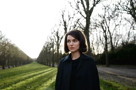 Woman in a dark coat stands on a tree-lined avenue at dusk; 5K Ultra HD desktop wallpaper inspired by the 2016 film Jackie.