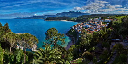 HD desktop wallpaper of a Spanish coastal town with a vibrant ocean, palm trees, houses, and a lush landscape under a blue sky.