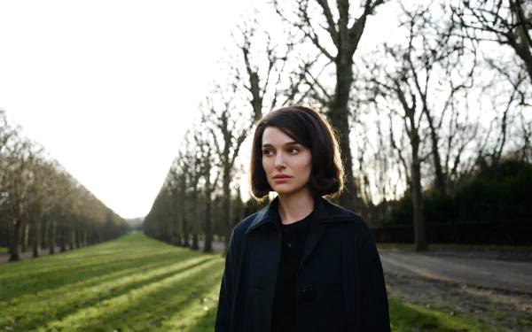 Woman in a dark coat stands on a tree-lined avenue at dusk; 5K Ultra HD desktop wallpaper inspired by the 2016 film Jackie.