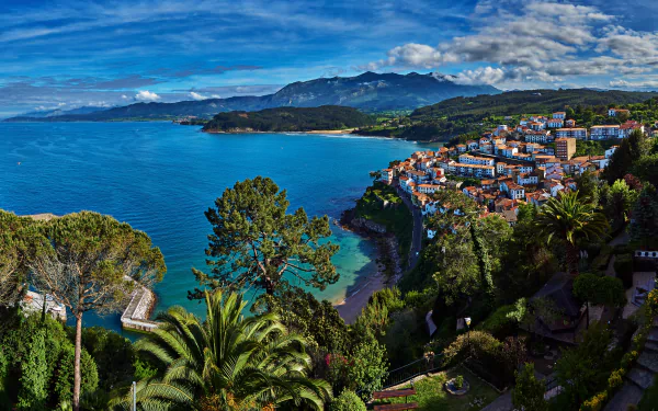 HD desktop wallpaper of a Spanish coastal town with a vibrant ocean, palm trees, houses, and a lush landscape under a blue sky.