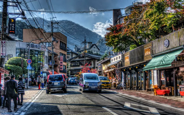 A vibrant street scene in Kobe, Japan, featuring cars on the road, distinctive architecture, and lush greenery against a backdrop of mountains. This HD desktop wallpaper captures the essence of urban life in HDR.