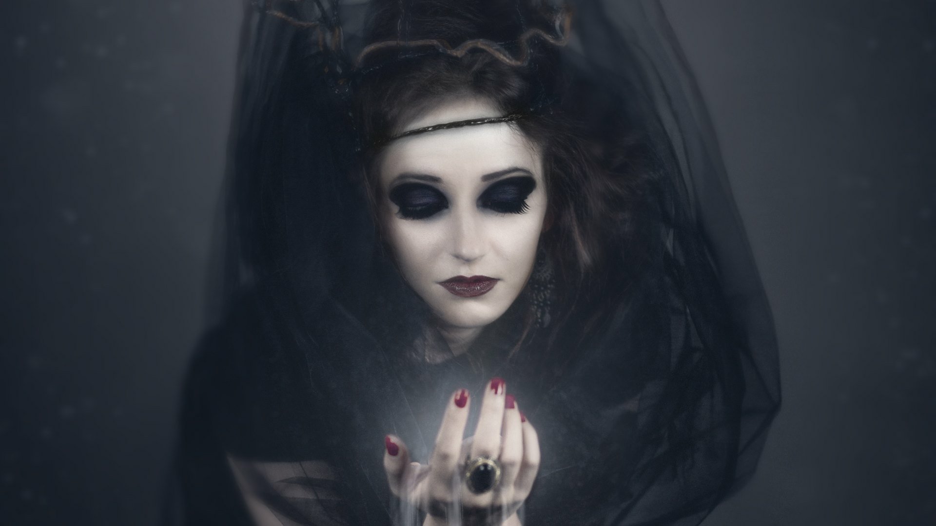 HD PC desktop wallpaper: dark fantasy vampire witch in a black veil, pale face with heavy dark eye makeup, red lipstick and nails, cradling a glowing orb as a moody background.
