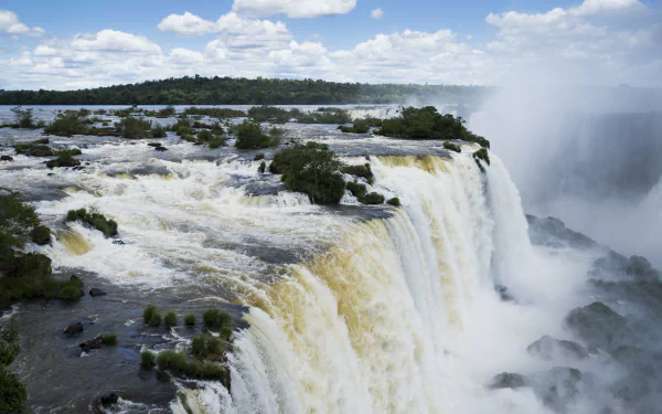 A stunning 4K Ultra HD wallpaper showcasing the powerful Iguazu Falls cascading through lush nature under a partly cloudy sky.