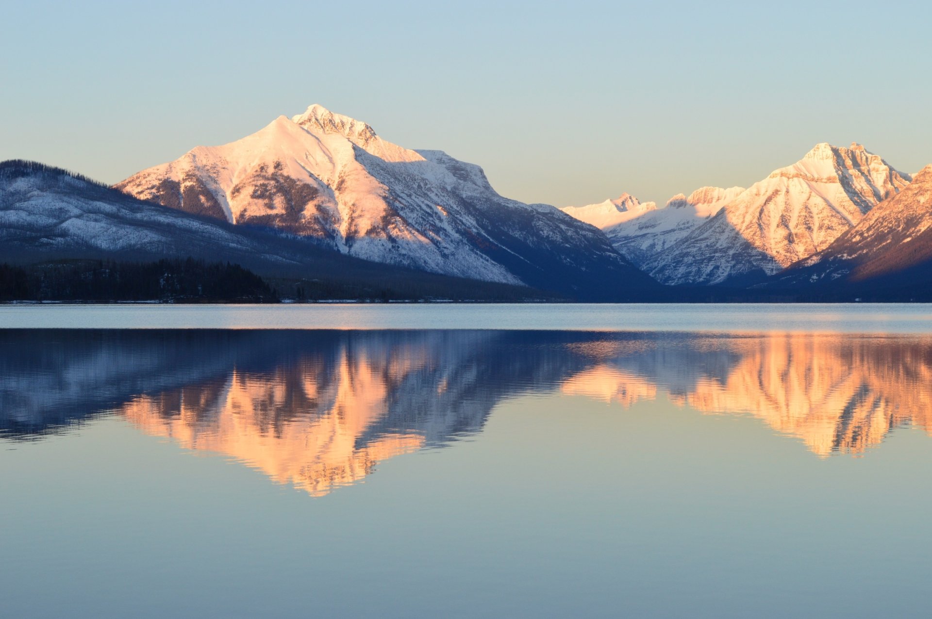 Winter view of snow-capped mountains reflecting on the calm waters of Lake McDonald in Glacier National Park, Montana, USA.