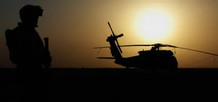 Silhouette of a soldier next to a Sikorsky UH-60 Black Hawk helicopter, set against a vibrant sunset. This HD image captures a moment in military aviation.