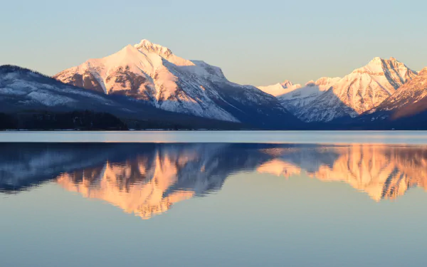 Winter view of snow-capped mountains reflecting on the calm waters of Lake McDonald in Glacier National Park, Montana, USA.