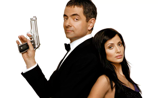 HD desktop wallpaper: two actors back-to-back on a white background — man in a tuxedo holding a pistol, woman in a black dress, cinematic movie poster/spy-comedy vibe.
