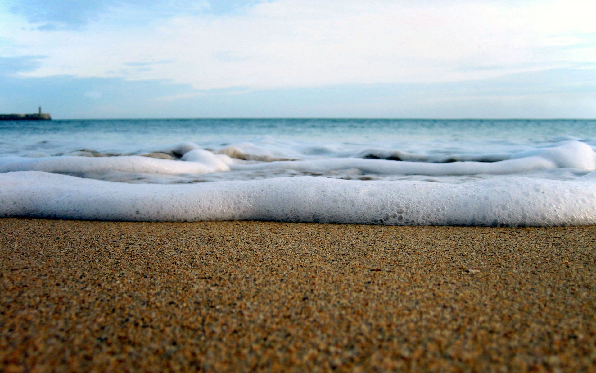 HD PC desktop wallpaper showing gentle ocean waves rolling onto a sandy beach under a calm, partly cloudy sky, capturing serene natural coastal beauty.