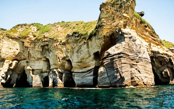 A striking cliffside along a serene shoreline, with clear blue ocean waters lapping against the rugged rock formations, showcasing the beauty of nature.