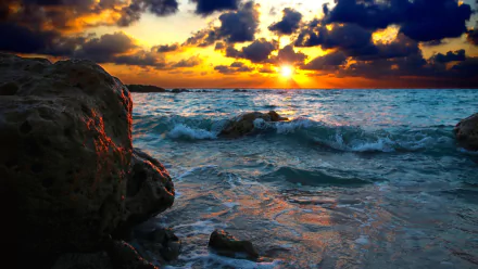 HD desktop wallpaper featuring a stunning sunset over the ocean horizon, with waves crashing against rocky shores, capturing the beauty of nature.