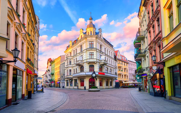 HD desktop wallpaper of a picturesque city square in Poland, featuring stunning architectural buildings with pastel facades under a blue sky with pink clouds.