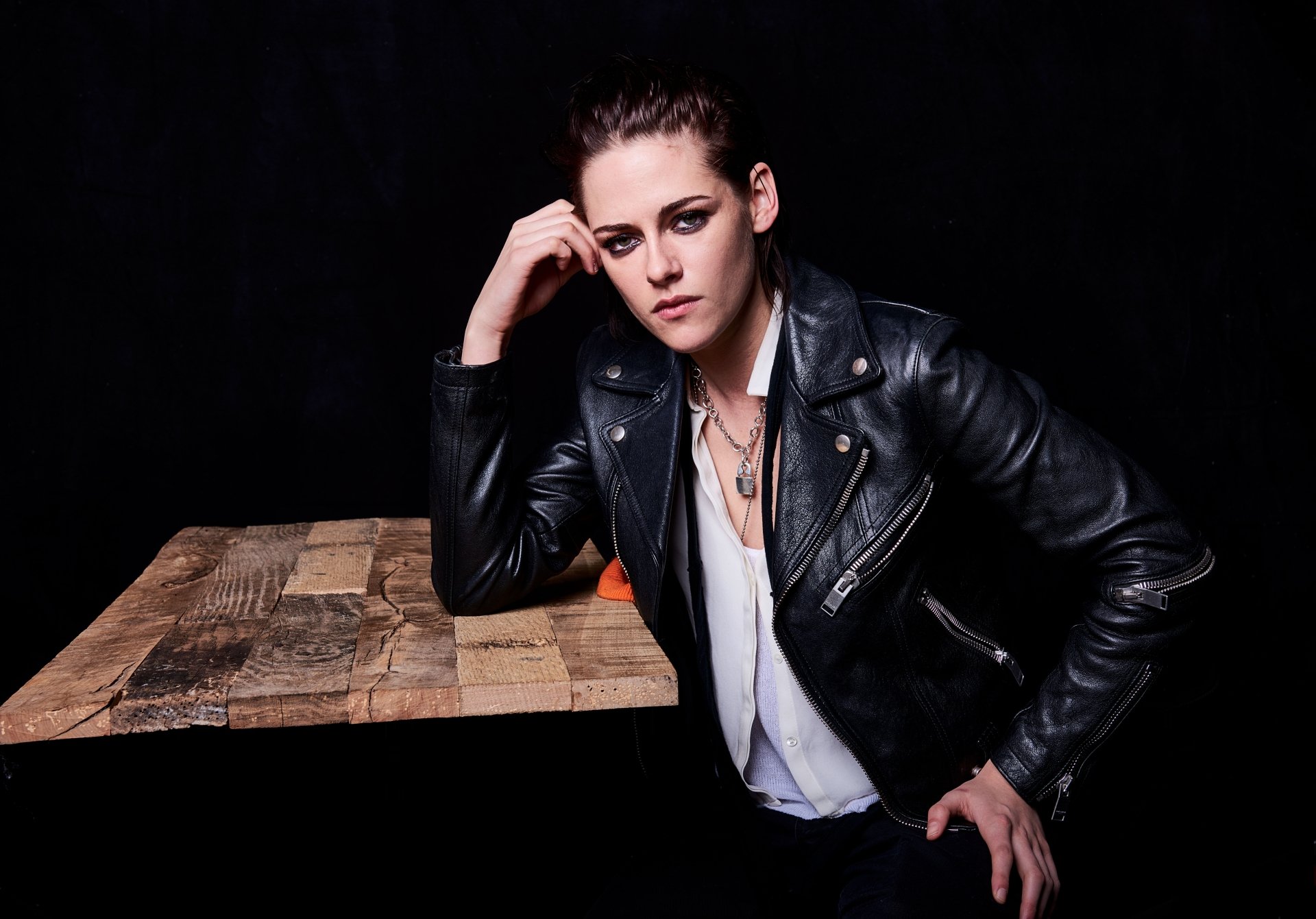 Portrait of American actress Kristen Stewart with brunette hair and green eyes, wearing a black leather jacket, set against a dark background in 8K Ultra HD quality.